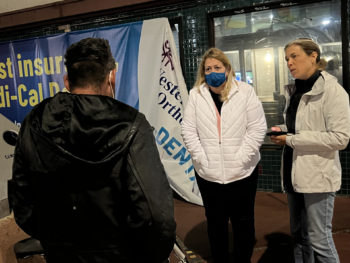 two women talk to a homeless man