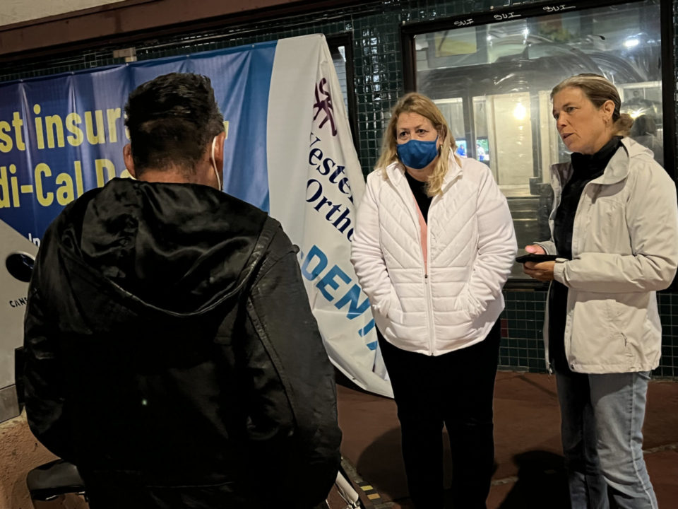 two women talk to a homeless man