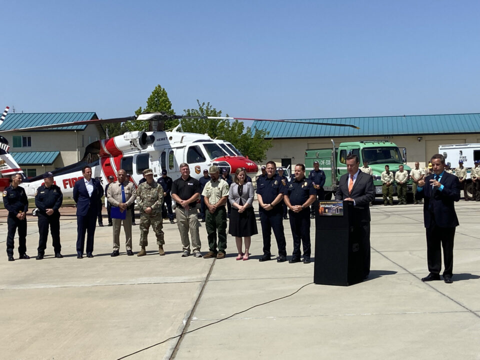 Supervisor Joel Anderson speaking at a CAL FIRE event on wildfire preparedness standing in front of fire crews, a brush fire truck and a fire helicopter