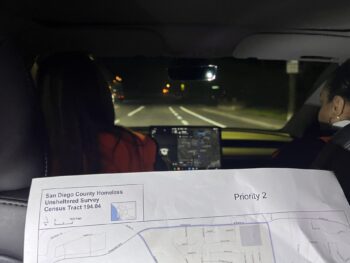 a person holds a map and the backside of a car with two people in the front seat