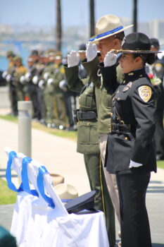 3 officers stand at salute in front of 3 empty chairs