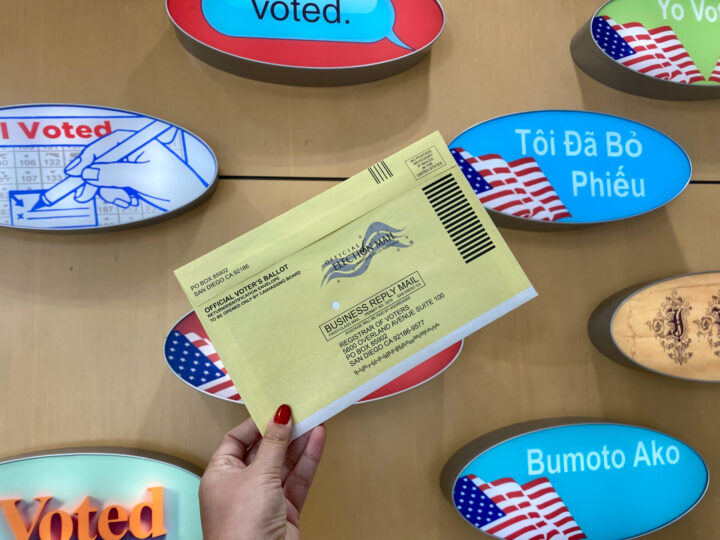 Hand holding mail in ballot in front of "I voted" stickers.