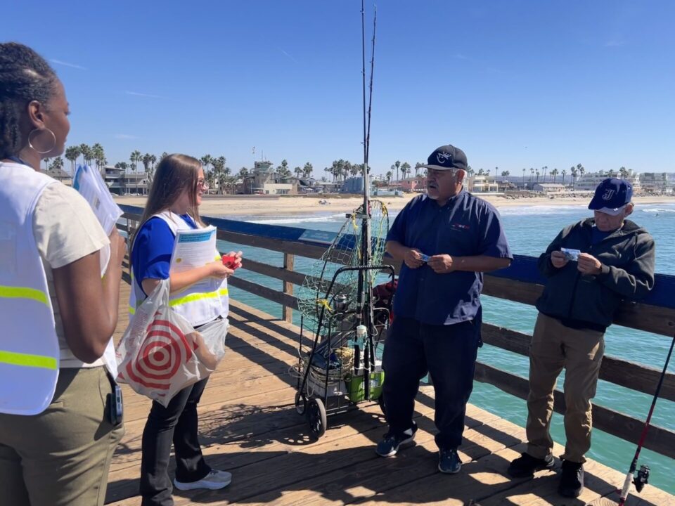 Two CDC workers in white vests speak with two male fishermen