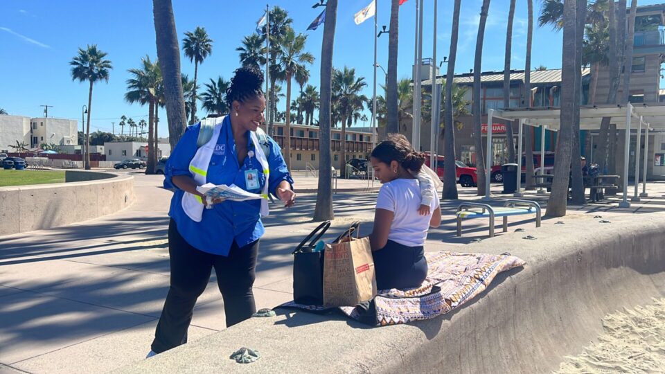 CDC volunteer handing ACE Survey flyer to woman holding child sitting on a bench