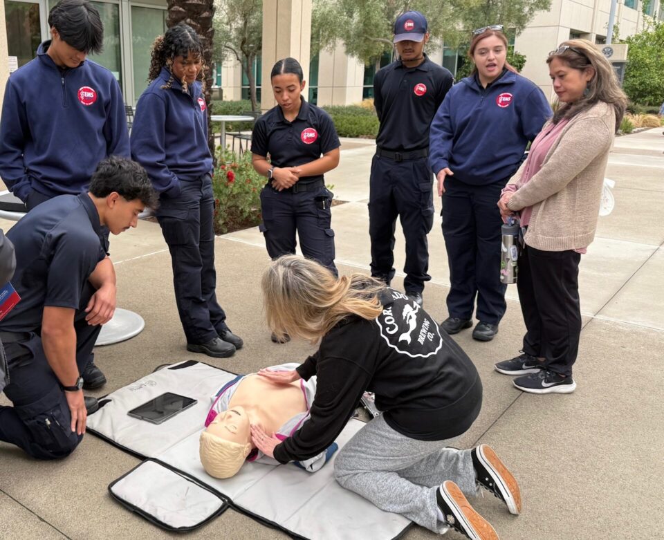 EMS Corps students help with hands only CPR on a soft pad with a training doll