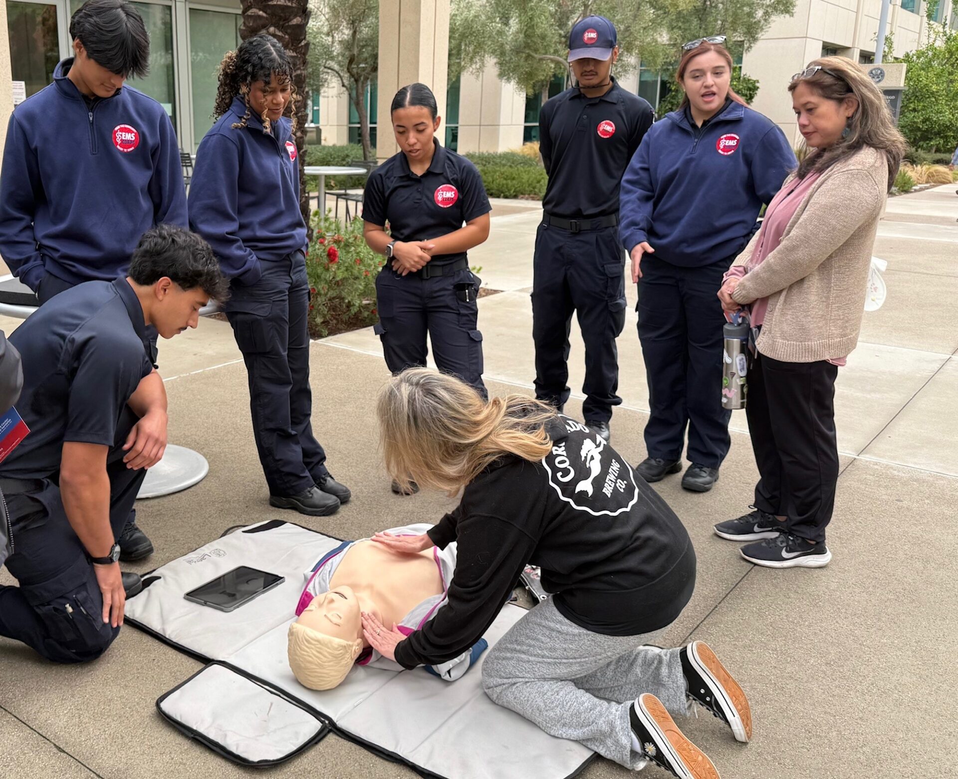 EMS Corps students help with hands only CPR on a soft pad with a training doll