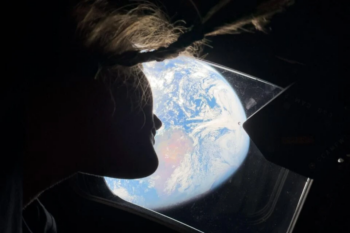 Female astronaut looking out window of space capsule at Earth