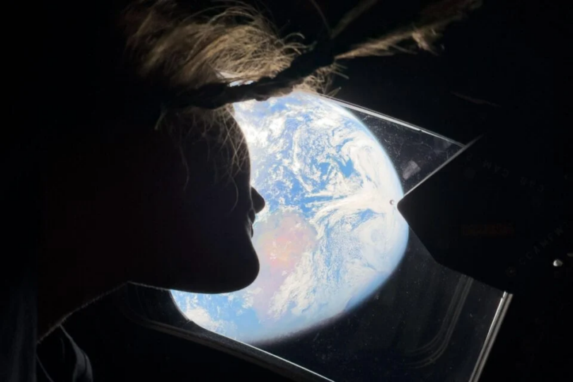 Female astronaut looking out window of space capsule at Earth