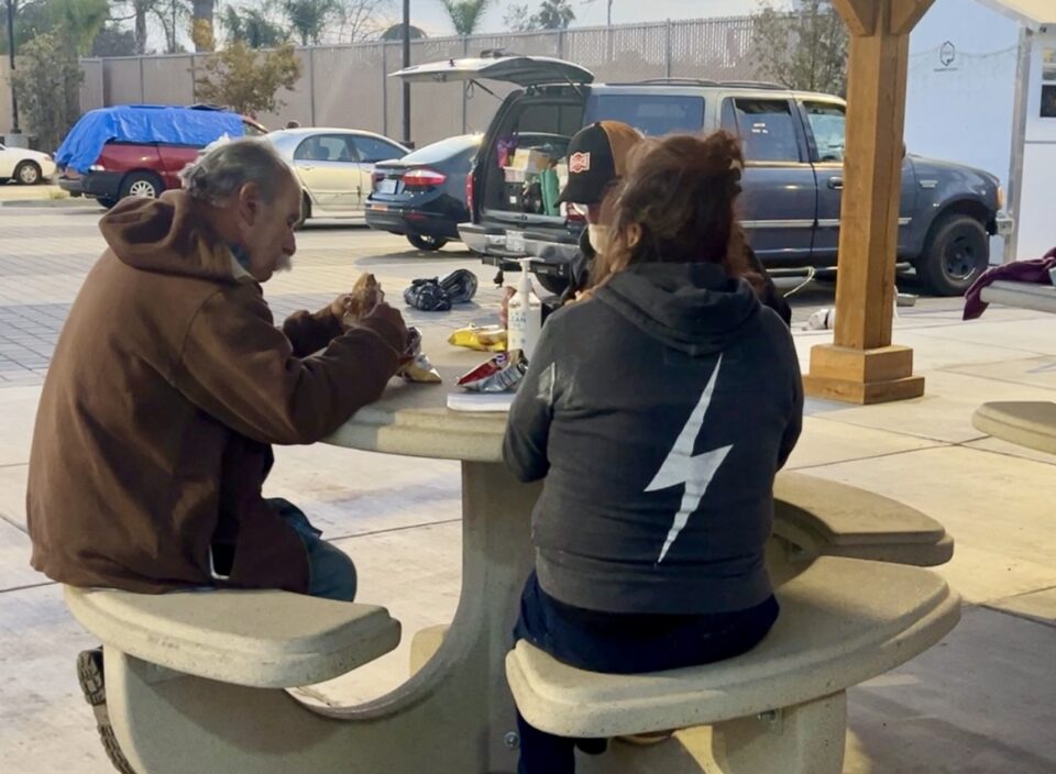 three people sit at picnic table in parking lot