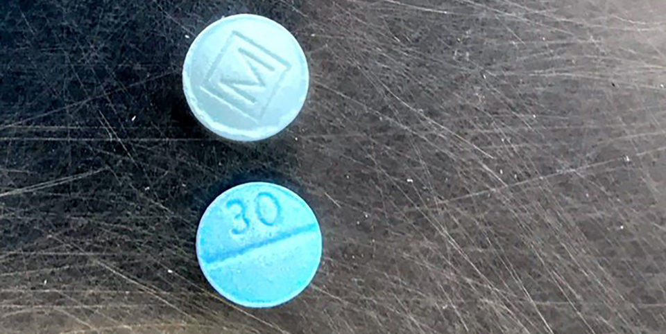 Two blue round pills with an M etched on one and 30 on the other. The pills are counterfeit oxycodone.