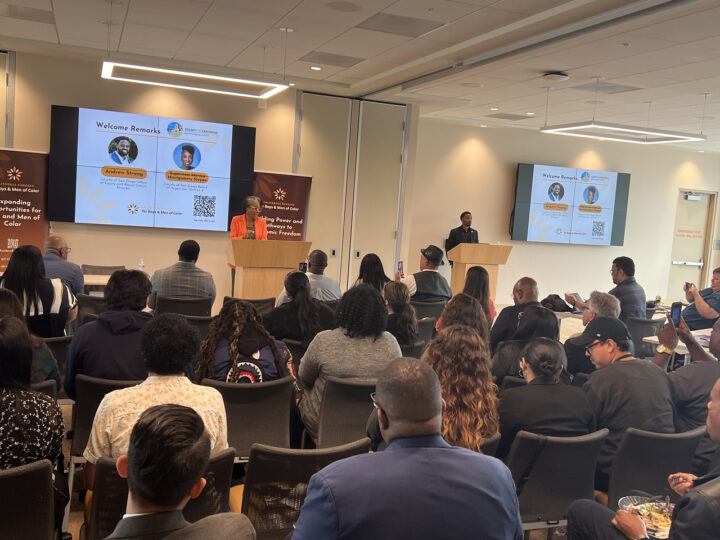 a presenter stands a a podium with a large audience in a meeting room
