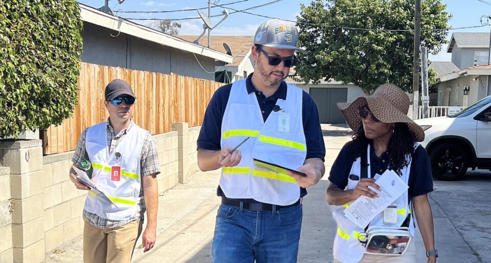 Three volunteers in white reflective vests walk and review information on clipboard