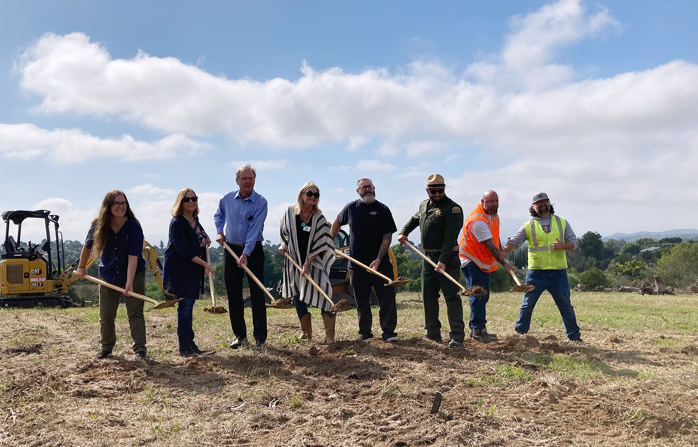 8 people hold shovels in a field