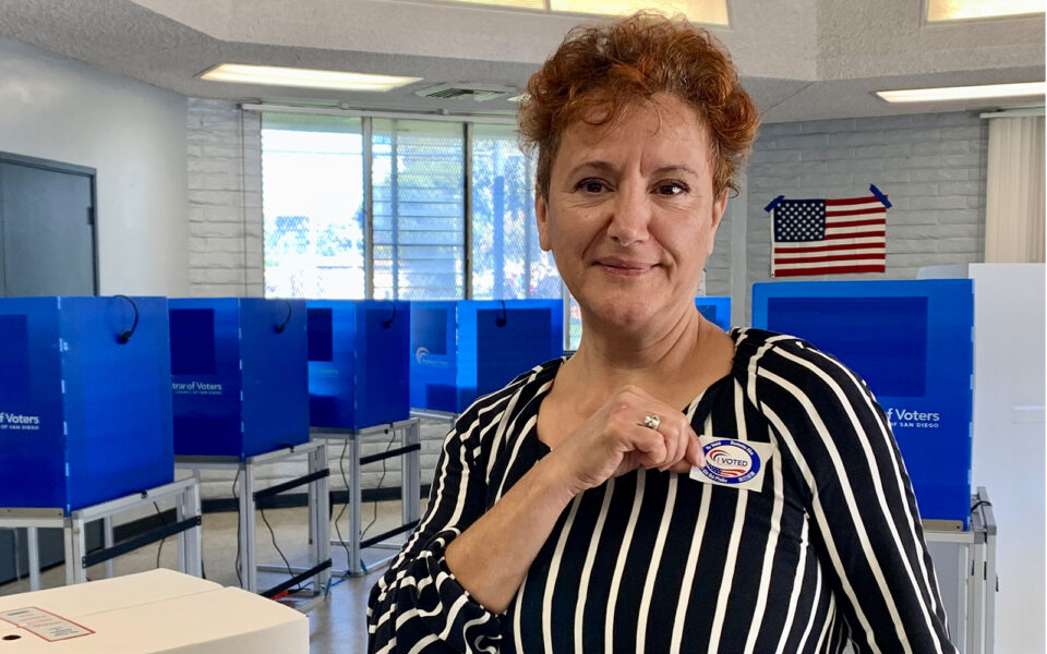 woman holds sticker up to shirt in a voting center