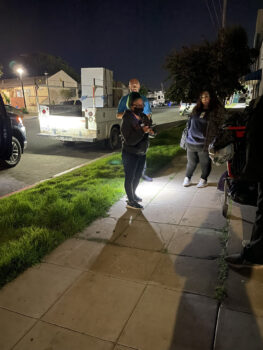 three people stand on the sidewalk at night