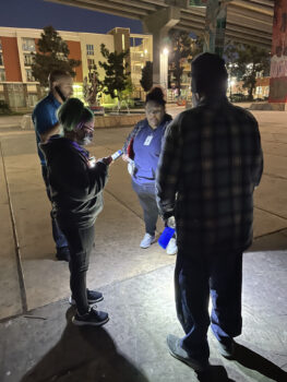 four people standing near an overpass speak to each other in a circle