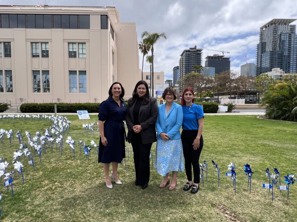 4 people stand on lawn with pinwheels in ground