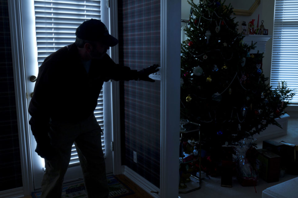 Burglar creeping around a home with a decorated Christmas tree.