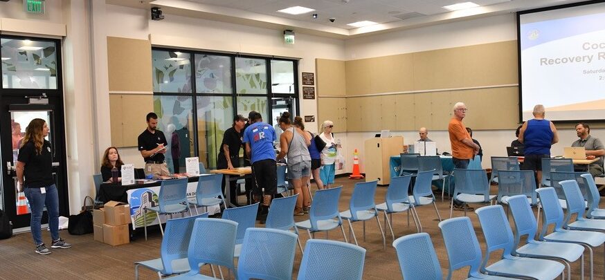 People standing and speaking in front of tables in a room at the Lakeside Library