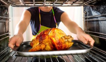 a woman places a turkey into the oven