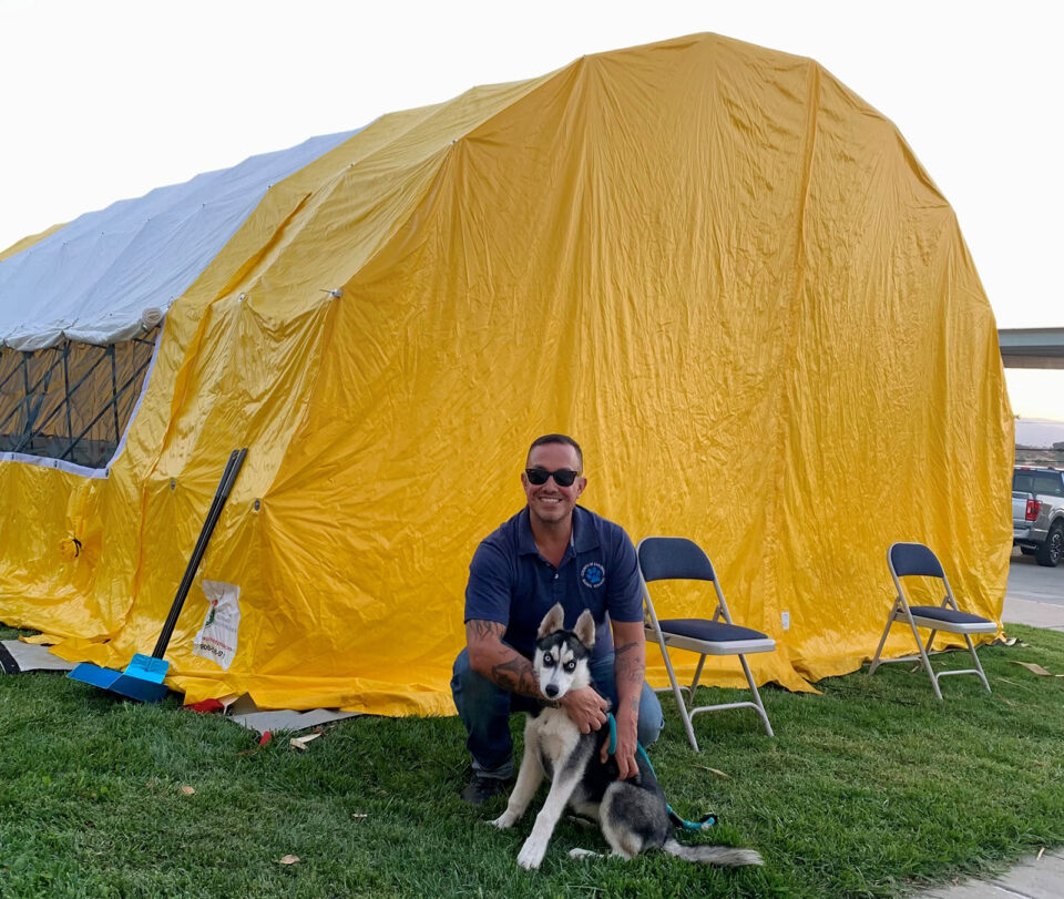 Animal Services attendant poses with dog outside evacuation tent.
