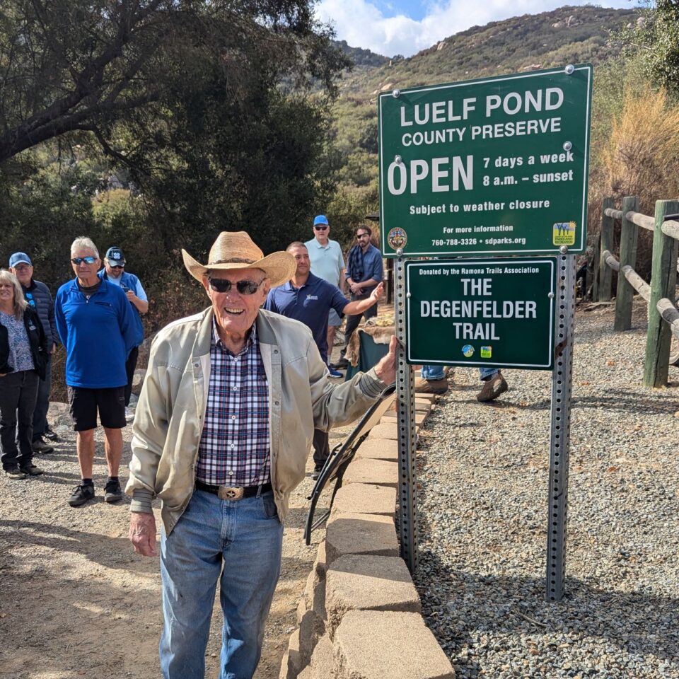 person with hat on leans against Luelf Pond County Preserve trail sign