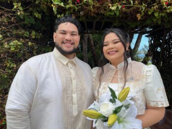 Couple stands under arch of vines and flowers