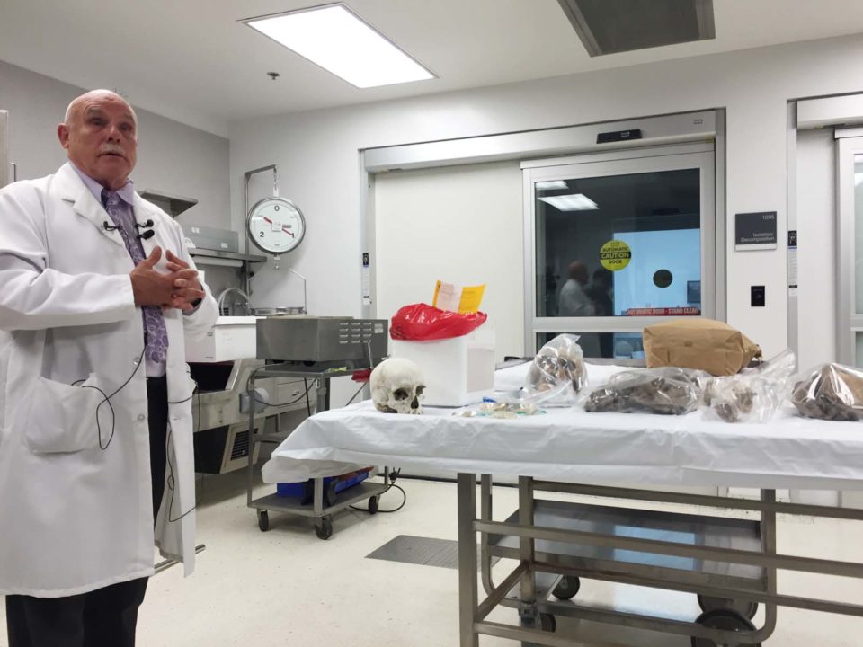 Chief County Medical Examiner in an examining room with skull on table.