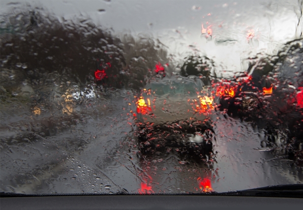 Windshield view of rainy road with cars in front.