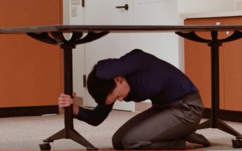 Woman under a table, holding a table leg, covering head.
