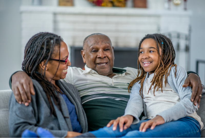 A family of three sit and smile on the couch