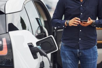 man stands near an electric car that is charging
