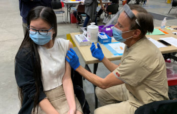 A teenage girl looks away as she is about to receive her COVID-19 vaccine.