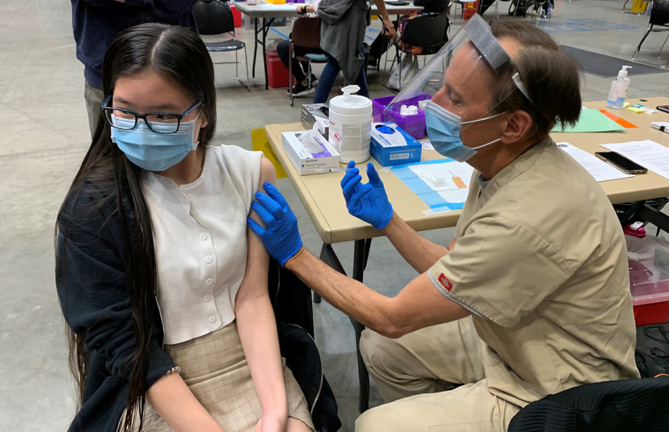 A teenage girl looks away as she is about to receive her COVID-19 vaccine.