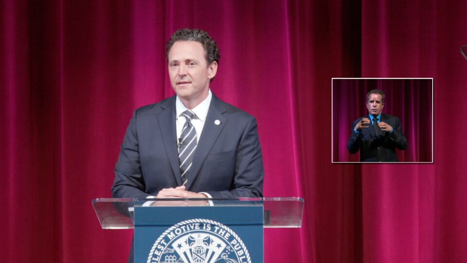 Nathan Fletcher stands at podium, ASL translator in picture in picture