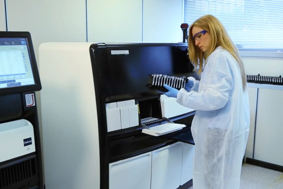 Woman in lab coat in front of black and white machine.