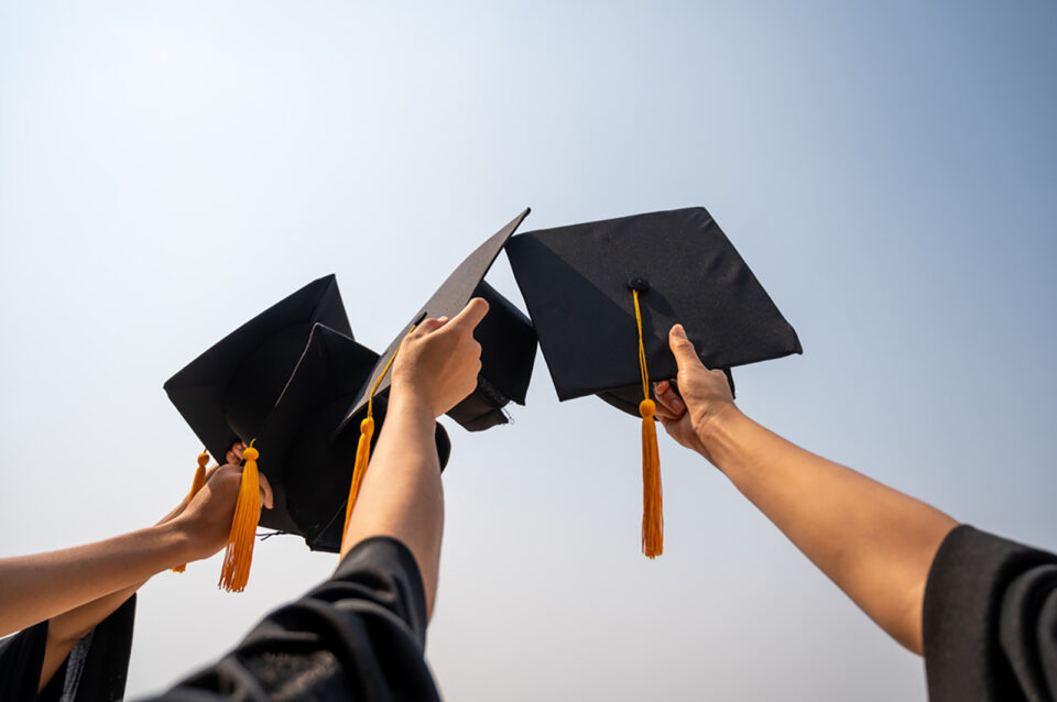 Arms holding up 4 Graduation caps to the sky