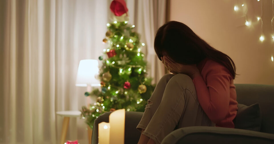 woman holding face in sadness by holiday tree