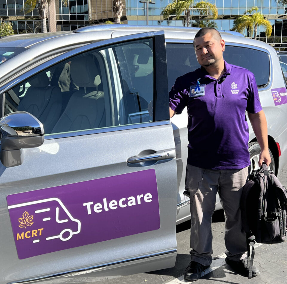 Mobile Crisis Response Team member dressed in purple uniform shirt standing in front of a silver van used in the service