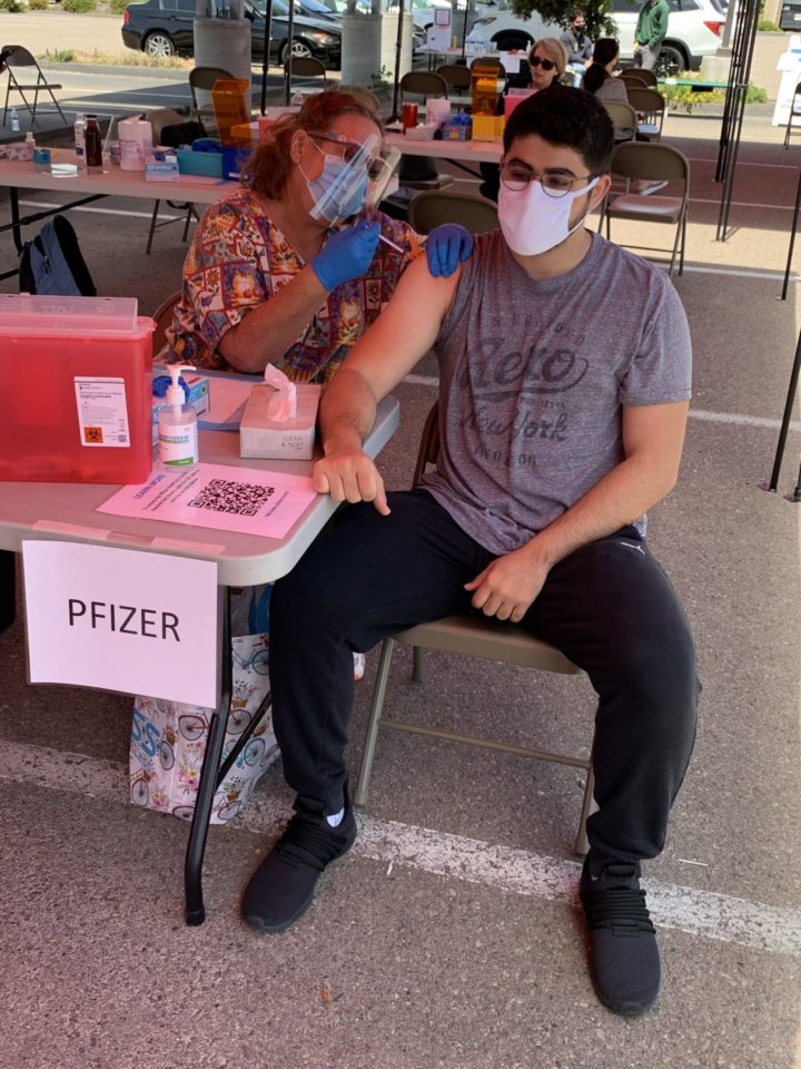 young man sits on a chair while a woman gives him a vaccine