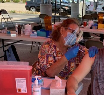 young man sits on a chair while a woman gives him a vaccine