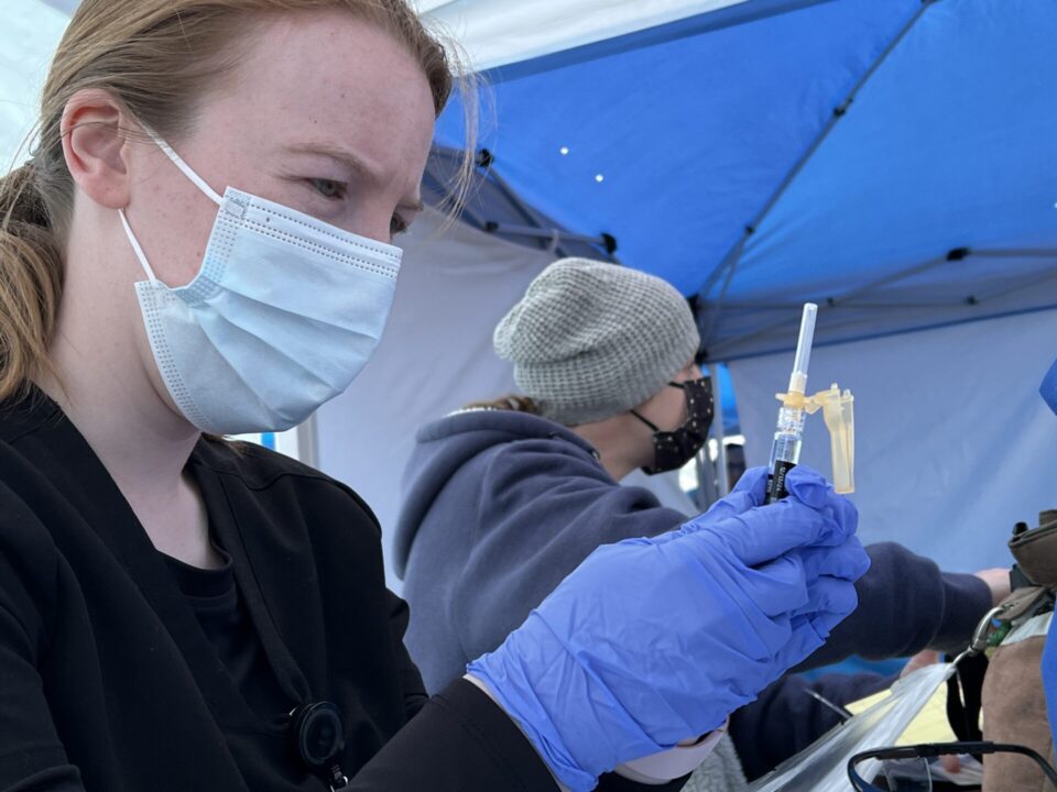 Public Health nurse wearing mask looks at vaccine