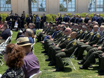 People sit in folding chair and some stand for a ceremony