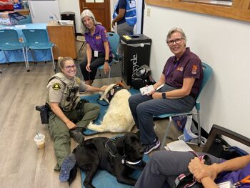 A deputy sits on the floord with a two dogs
