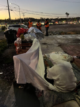a person sits on the ground next to items covered with a blanket