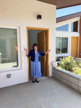 Senior resident holding out her arms in front of her front door