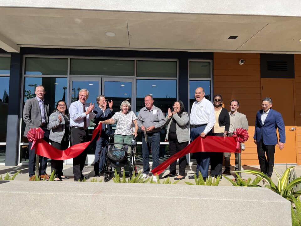 people smiling as red ribbon that was just cut by gold sissors falls