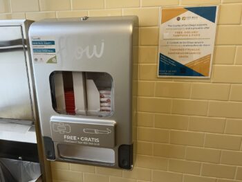 Tampon and pad dispenser on yellow tile bathroom wall