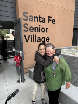 Two senior women hugging in front of new housing complex