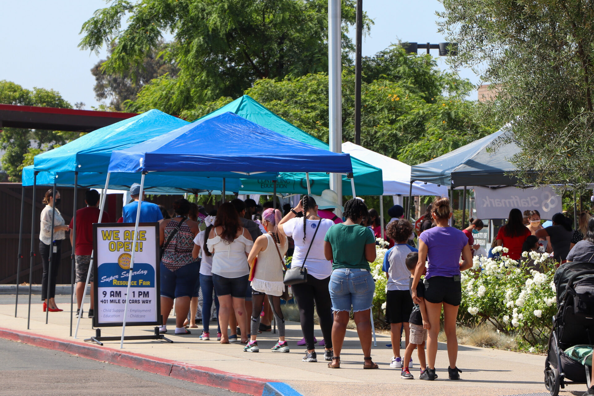 People waiting outside blue pop up tents for child support services at San Diego County Department of Child Support Services Super Saturdays event